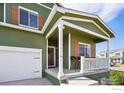 Inviting porch with white railing, dark wood door with wreath, and green siding that enhances curb appeal at 1157 Savona Ave, Fort Lupton, CO 80621