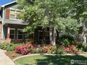A lush front yard featuring mature trees, colorful flower beds, and a well-maintained lawn leading to a cozy covered porch at 1715 Wales Dr, Berthoud, CO 80513