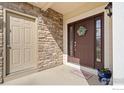 Close-up of the front porch with stone siding, a brown front door, and a cozy welcome mat at 11676 Montgomery Cir, Longmont, CO 80504