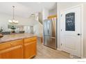 Bright kitchen with stainless steel refrigerator, wood cabinets, adjacent to a staircase, and hardwood flooring at 1453 Woodcock St, Berthoud, CO 80513