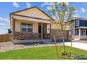 Inviting single-Gathering home featuring a cozy front porch, a well-maintained lawn, and stone accents on the facade at 2218 Crosswind St, Fort Lupton, CO 80621