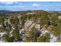 Expansive aerial view of elegant home nestled in a dense forest, featuring snow-dusted landscape and mountain views at 1682 Montane E Dr, Golden, CO 80401