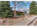 View of the front of the house with trees and partial snow-covered gravel yard at 10249 W Grand Ave, Littleton, CO 80127