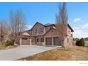 Charming home features a three-car garage with stone accents, a well-maintained lawn, and a welcoming entrance at 14958 Wistera Way, Broomfield, CO 80023