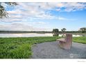 Scenic pond view with a stone bench, surrounded by lush greenery and a clear blue sky with clouds at 3796 Vale View Ln, Mead, CO 80542