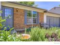 Close-up of brick exterior with blue door, window with shutters, and a bench surrounded by plants at 308 Baron Ave, Lafayette, CO 80026