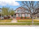 Charming two-story home with a brick foundation, manicured lawn, and mature trees at 5355 Killdeer St, Brighton, CO 80601