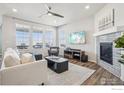 Bright living room featuring hardwood floors, white walls, gas fireplace, modern ceiling fan, and large windows with views at 3047 Grizzly Peak Dr, Broomfield, CO 80023