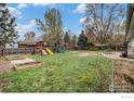 Large backyard with wooden playset, garden beds, mature trees, and grassy area at 339 Indiana Ave, Berthoud, CO 80513