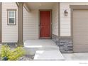Close up of the front entrance with a red door, stone accents, and green landscaping at 6131 Easton Cir, Frederick, CO 80504