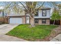Charming two-story home with a brick facade, attached garage, a well-manicured lawn, and mature trees at 13755 W 65Th Dr, Arvada, CO 80004