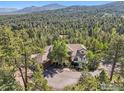 Aerial view showcases the property's nestled setting amidst a dense forest and distant mountains at 27921 Alabraska Ln, Evergreen, CO 80439