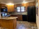 Well-equipped kitchen with wood cabinets, a black fridge, an island, and views from the window at 843 Sumner St, Longmont, CO 80501