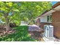 Brick home exterior featuring stone patio, green grass, mature trees, and a modern AC unit at 700 33Rd St, Boulder, CO 80303