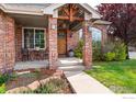 Inviting front porch with brick columns, decorative wood beams, and seating area, creating a cozy entrance at 13042 Logan St, Thornton, CO 80241