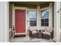 Cozy porch area with two chairs, a small table, and a red front door at 15800 E 121St Ave # 4K, Brighton, CO 80603