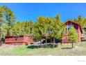 View of the rustic home with unique exterior, trees, and sloping grass yard with blue skies above at 548 Coughlin Meadows Rd, Boulder, CO 80302