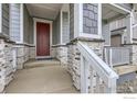 Inviting front porch features stone accents, a red door, and white railings for a welcoming entrance at 5891 Aspenglow St, Longmont, CO 80504