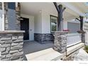 Cozy covered porch with stone columns, white railings, and a black front door, perfect for relaxing outdoors at 1923 High Plains Dr, Longmont, CO 80503