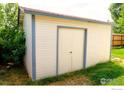Exterior view of a shed, featuring white siding, a light-colored door and blue trim at 730 Douglas Pl, Berthoud, CO 80513