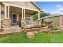 Inviting front porch with stone columns, a white railing, and decorative landscaping at 1831 Ashford Cir, Longmont, CO 80504