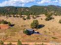 An aerial view captures a charming hillside home featuring a sprawling landscape, driveway, and mountain views at 6465 Red Hill Rd, Boulder, CO 80302