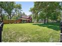 Expansive yard with lush green grass, mature trees, and a charming red home in the background at 1245 Longs Peak Ave, Longmont, CO 80501