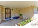 Inviting covered front porch with brick walls, decorative iron door, bench, and flower bed at 3375 Zephyr Ct, Wheat Ridge, CO 80033