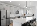 Modern kitchen featuring gray cabinets, stainless steel appliances, a large island with seating, and stylish pendant lighting at 12155 W 57Th Pl, Arvada, CO 80002