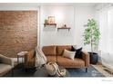 Stylish living room featuring a leather sofa, brick wall, shelves, greenery, and a comfortable sitting area at 135 E 8Th Ave, Denver, CO 80203