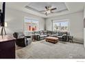 Comfortable living room with tray ceiling, ceiling fan, a sectional sofa, ottoman, and lots of light at 6150 Bluestem Grn, Frederick, CO 80530