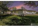 A well-manicured lawn surrounds this lovely home with a detached garage and fenced yard at dusk at 10635 County Road 24, Fort Lupton, CO 80621