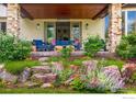 Covered patio with stone pillars featuring comfortable blue seating, decorative pillows, and blooming garden at 7205 Rustic Trl, Boulder, CO 80301
