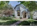 Charming two-story home with a quaint balcony, arched entryway, and a lush green lawn surrounded by trees at 1315 Gaylord St, Denver, CO 80206