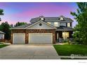Beautiful two-story home with a three-car garage, stone facade, and a manicured lawn at dusk at 14675 Golden Eagle Run, Broomfield, CO 80023