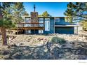 View of the back exterior highlighting the stone chimney and elevated wooden deck with natural surroundings at 8483 Thunderhead Dr, Boulder, CO 80302
