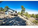 Side exterior shot showing a blue home with a stone chimney and wooden deck on a sunny hillside lot at 8483 Thunderhead Dr, Boulder, CO 80302