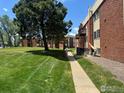 Exterior view of the building complex with green grass and lush trees on a sunny day at 3623 S Sheridan Blvd # 11, Lakewood, CO 80235