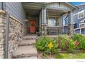 Inviting covered front porch with stone pillars, flower beds, and a cheerful pink front door at 1682 Crestview Ln, Erie, CO 80516