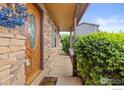 Inviting entryway with a wood door featuring a decorative glass insert, framed by stone and lush greenery at 112 Melody Ln, Platteville, CO 80651