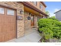 Welcoming entryway with a wooden front door, stone accents, and manicured bushes adding curb appeal at 112 Melody Ln, Platteville, CO 80651