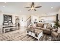 Open-concept living space featuring hardwood floors, stylish furniture, modern ceiling fan, and a staircase at 12889 Clearview St, Firestone, CO 80504