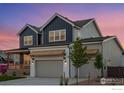 Side view of a two story home with a two car garage and covered front porch against a colorful evening sky at 1426 Swan Peter Dr, Berthoud, CO 80513