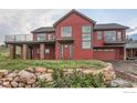 Striking red two-story home featuring modern windows, a front-facing garage, rock landscaping, and a covered porch area at 8241 N Foothills Hwy, Boulder, CO 80302