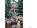 Picturesque waterfall feature cascading over rocks, surrounded by lush greenery and blue spruce trees at 6917 Timbers Dr, Evergreen, CO 80439