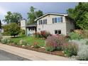 Charming two-story home with landscaped front yard featuring colorful flowers and green lawn at 6864 Balsam St, Arvada, CO 80004