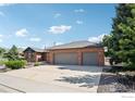 Spacious three-car garage with an expansive driveway, set against a backdrop of lush greenery at 1806 Crestone Ct, Longmont, CO 80504