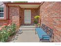 Cozy covered porch with a comfortable bench, hanging flowers, and decorative plants at 1443 Elmhurst Ct, Longmont, CO 80503