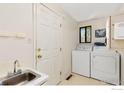 Functional laundry room with a washing machine, dryer, sink, storage cabinet, and outside access at 1323 Horizon Ln, Longmont, CO 80501
