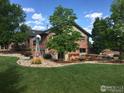 Backyard featuring a manicured lawn, mature trees, and stone landscaping around a brick home at 612 Joyce Ct, Berthoud, CO 80513